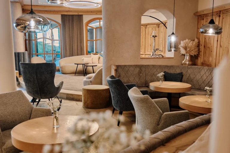Sessel und Holztische im Aufenthaltsbereich eines Hotels in Tirol, im Vordergrund Blumen